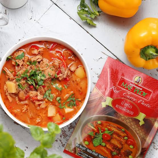 Mae Ploy red curry paste in a tub next to dried red chilies, garlic and lemongrass